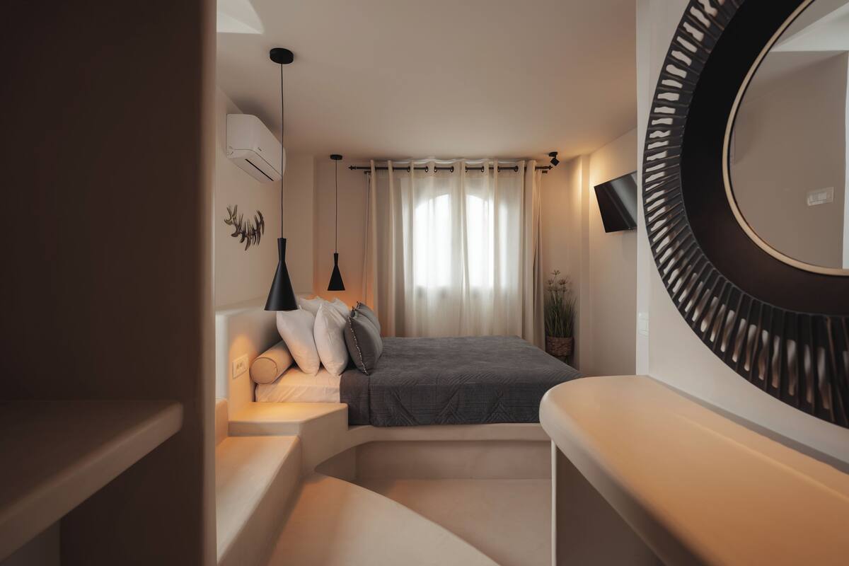 Un dormitorio moderno con una cama, lámparas de noche, un espejo redondo y un televisor en la pared.