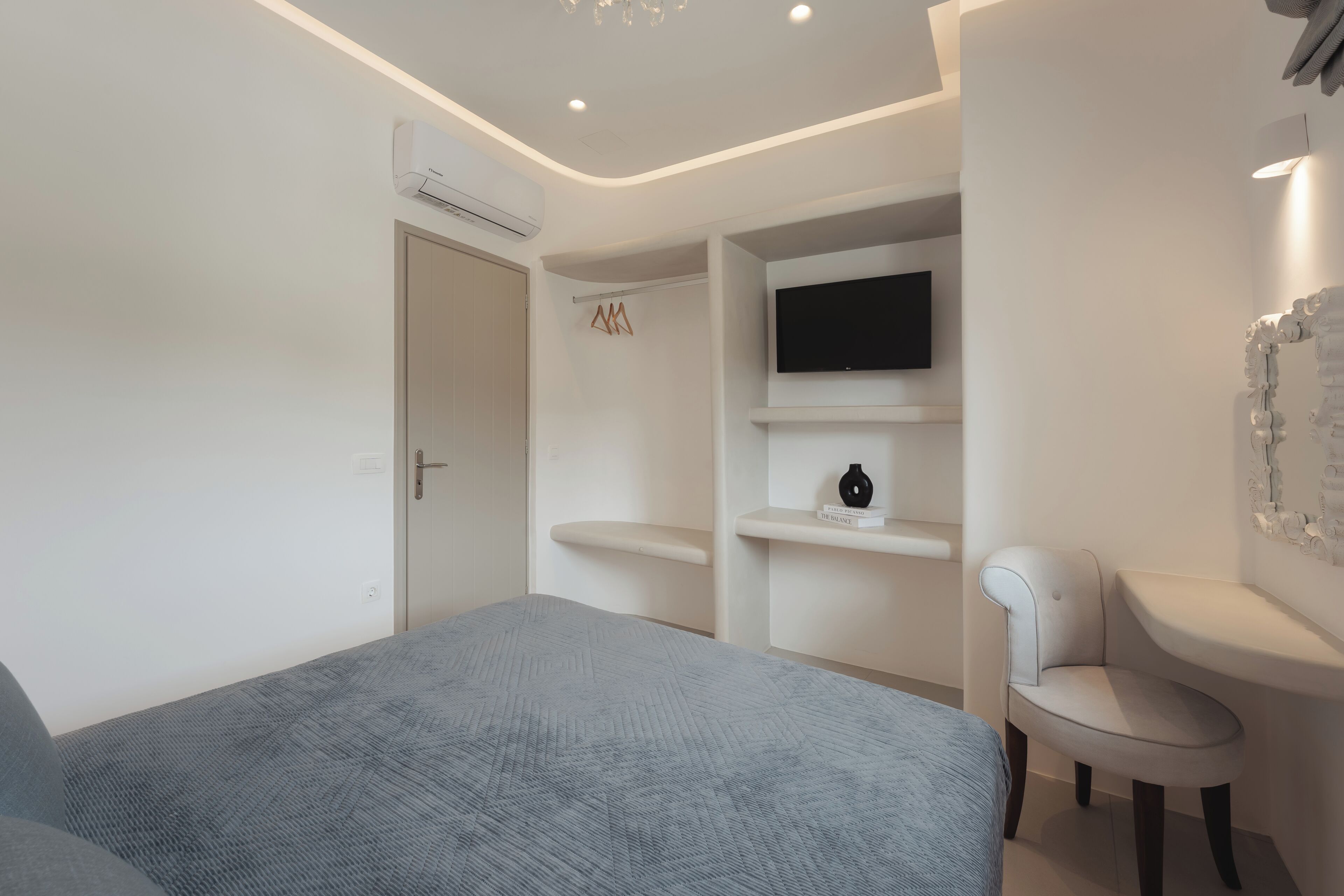 A modern bedroom with a bed, a TV mounted on the wall, a chair, and a shelf with a vase.