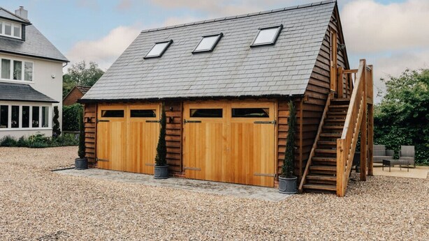 Une cabane en bois avec un toit en pente, deux portes de garage et un escalier en bois menant à l’entrée.