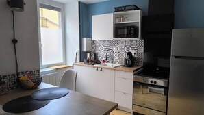 Eine kleine Küche mit Spüle, Herd und Kühlschrank. Ein Fenster sorgt für natürliches Licht, und die Wände sind mit gemusterten Fliesen verziert.