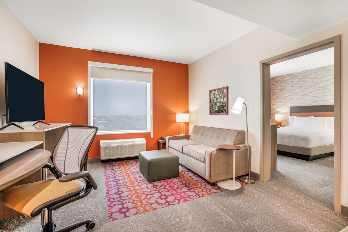 A hotel room with a desk, office chair, sofa, ottoman, and a bed.