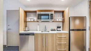 A compact kitchen with a built-in microwave, a stainless steel refrigerator, and a dishwasher. - Home2 Suites Hilton Aurora Medical Center (Aurora)