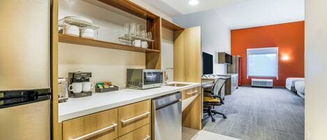 Una cucina moderna con forno a microonde, macchina del caffè e lavastoviglie integrate. C'è una zona con divano e televisore.