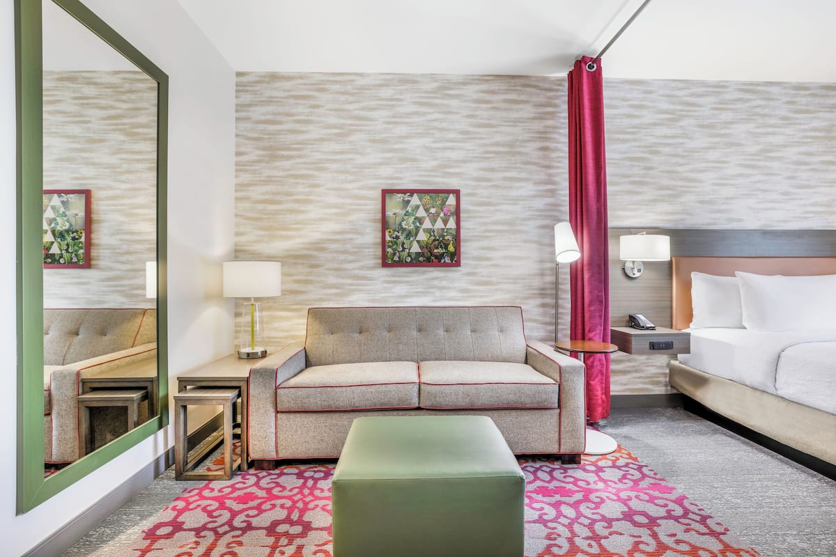 A hotel room with a sofa, a bed, a nightstand, a mirror, and a patterned rug.