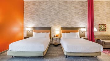 A hotel room with two beds, a small table with a lamp, a sofa, and a patterned wall.