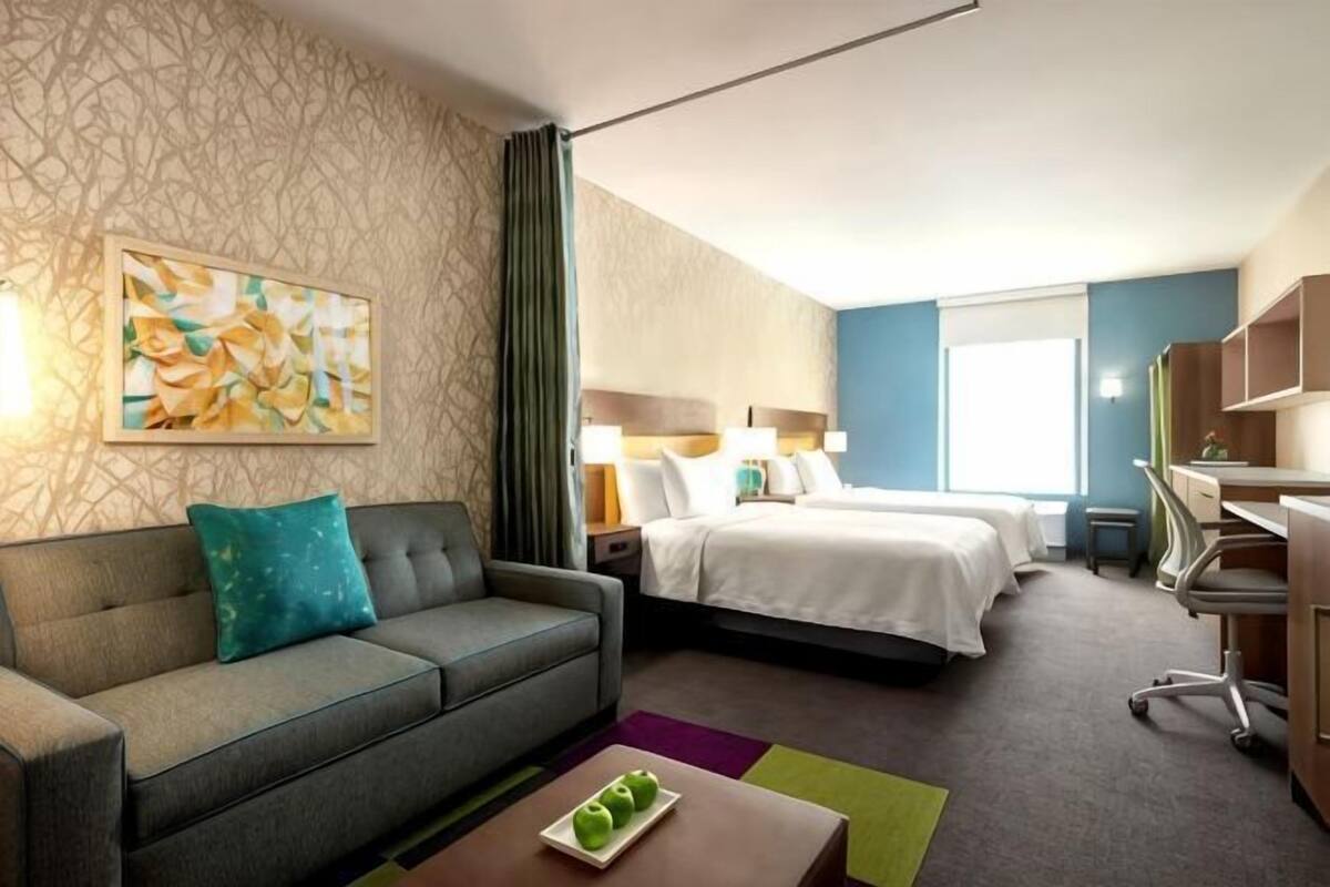 A hotel room with a sofa, a bed, a desk, and a painting on the wall.
