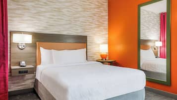 A hotel room with a bed, nightstand, lamp, and mirror.