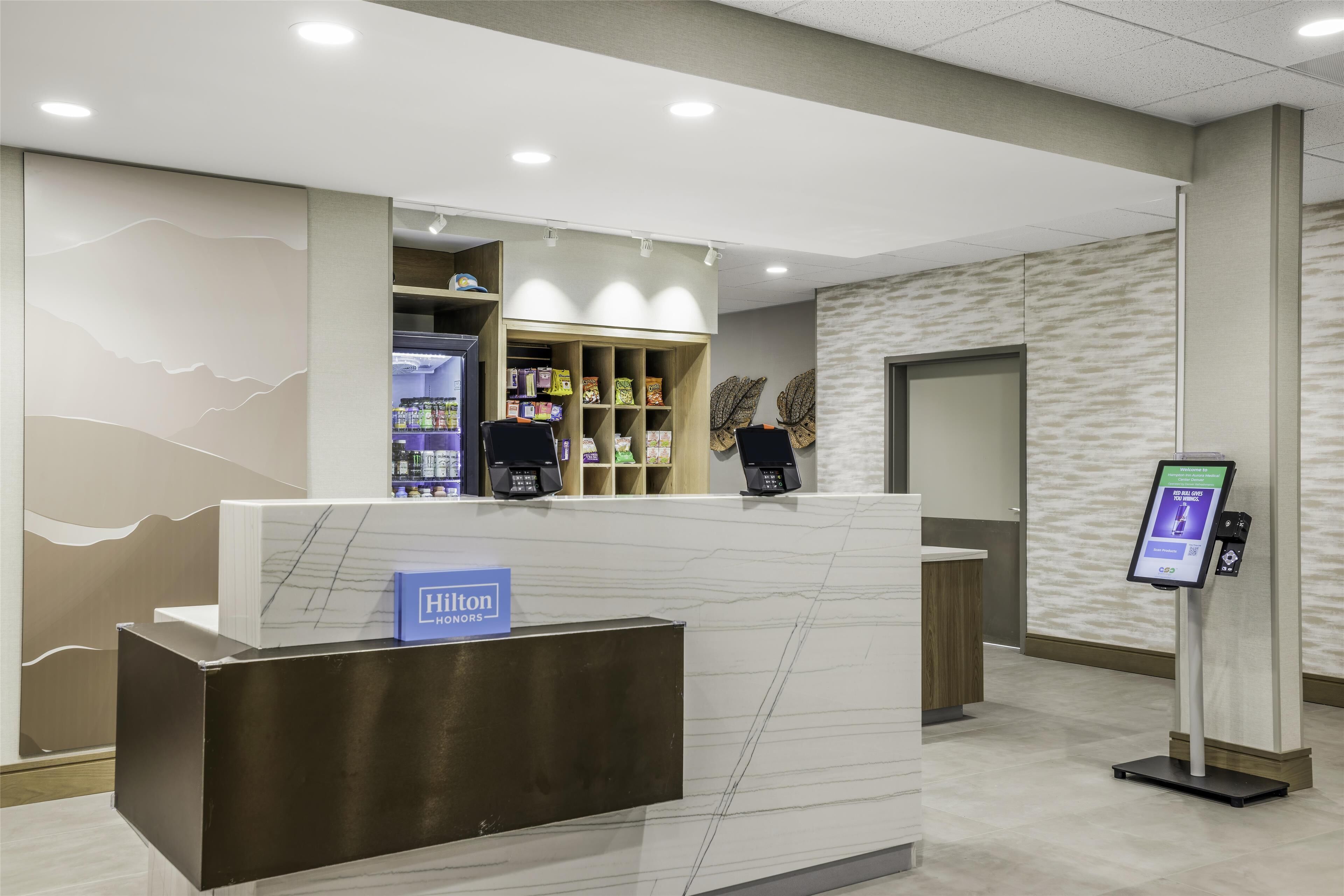 A reception desk with a 'Hilton' sign, a self-service kiosk, and a seating area with chairs.