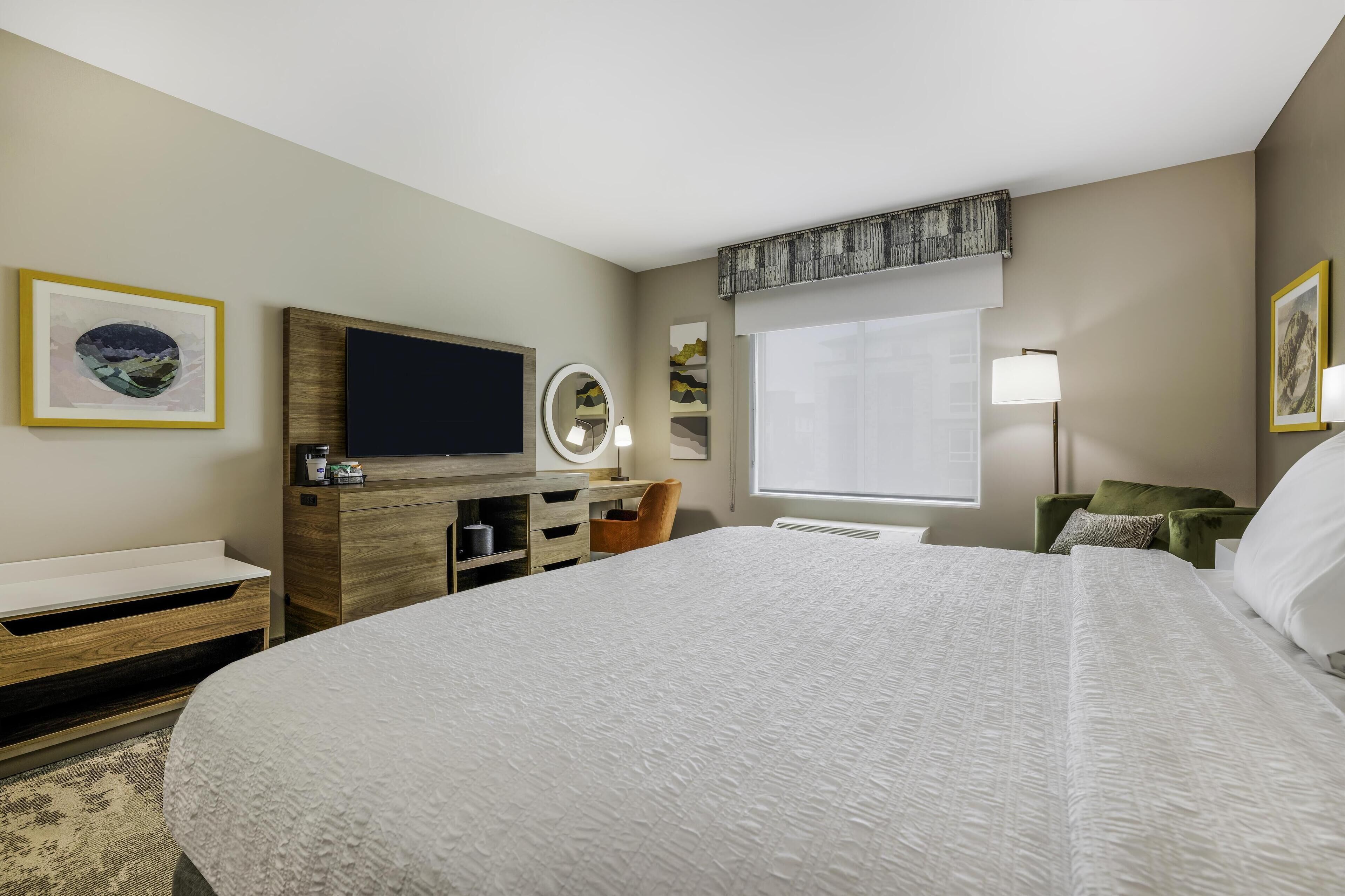 Une chambre d’hôtel avec un grand lit, une télévision, un bureau avec un miroir et une fenêtre donnant sur un beau paysage.