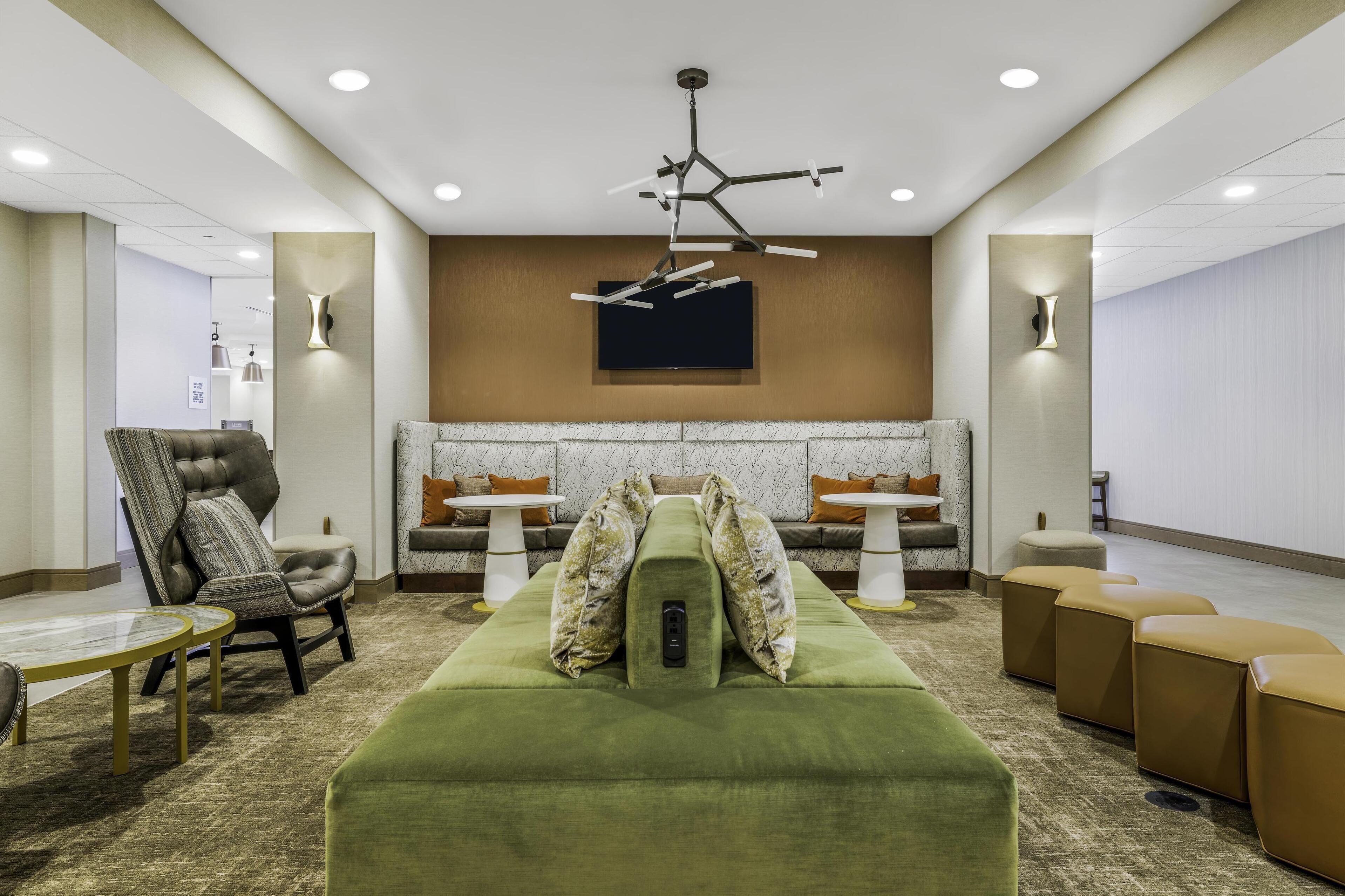 A modern lounge area with a green sofa, a tufted armchair, and a sectional sofa with patterned cushions.