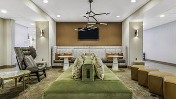 A modern lounge area with a green sofa, a tufted armchair, and a sectional sofa with patterned cushions.