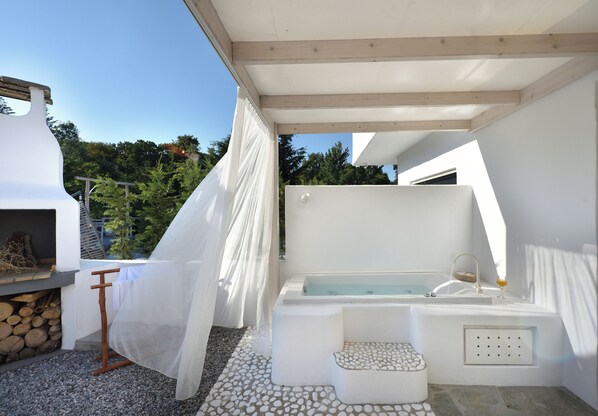 A spa area with a bathtub, a seating area, and a pergola with a white canopy. - Olympa Suites (Dio-Olympos)