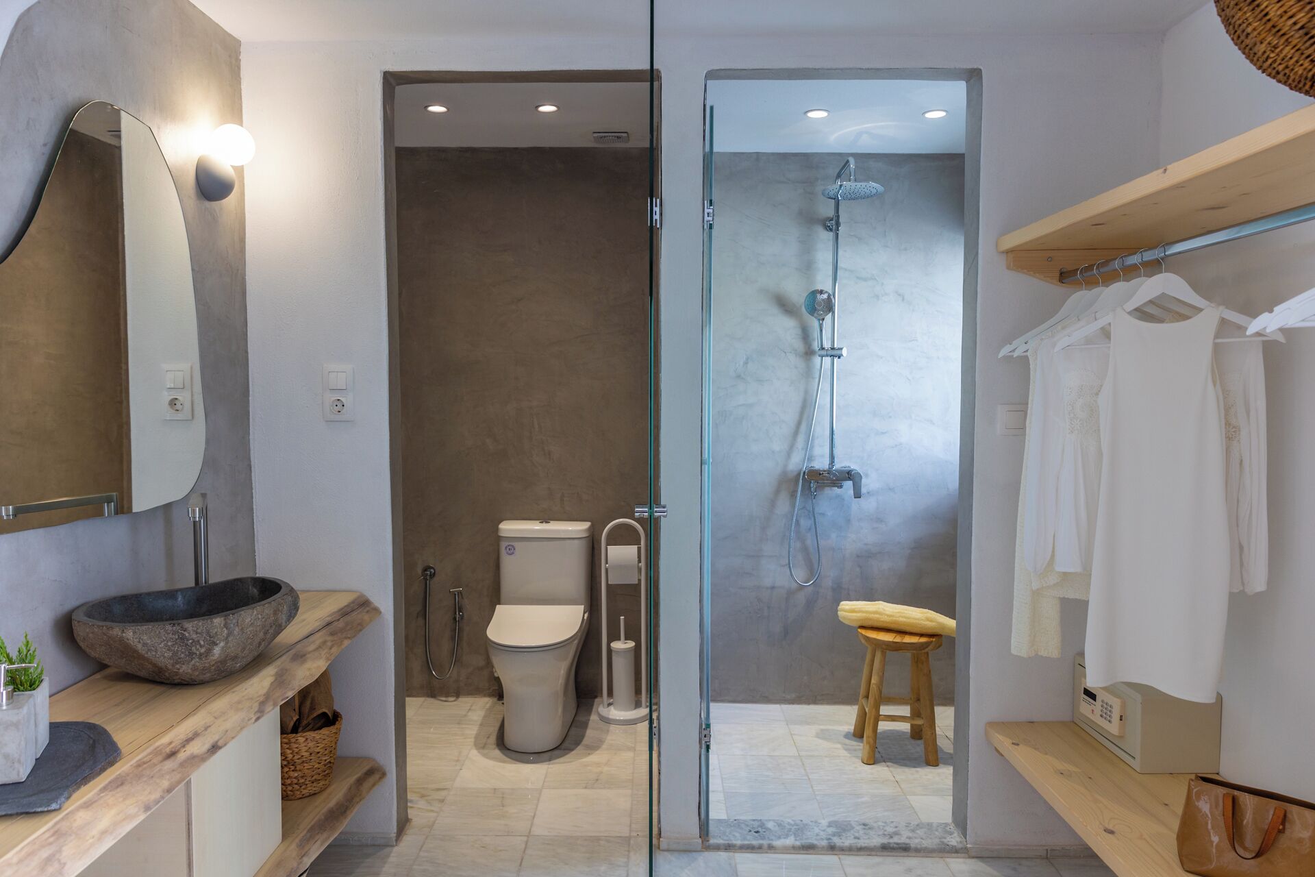 Un baño moderno con un espejo grande, un lavabo de piedra, un inodoro, una ducha y un taburete de madera.
