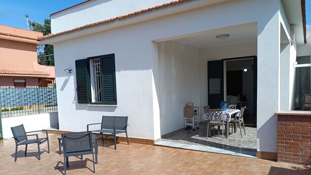 Un patio techado con una mesa, sillas, un carrito pequeño y una puerta que da a un espacio interior.