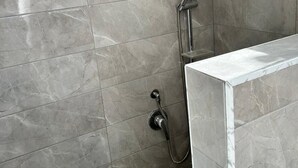 Un baño con baldosas de mármol gris, una ducha con cabezal de ducha manual y un lavamanos en esquina.