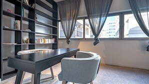 Et moderne værelse med et mørkt træskrivebord, en grå stol og en bogreol fyldt med bøger.