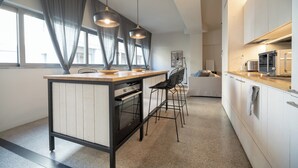 Et moderne køkken med en central ø, hængende lamper og udsigt til opholdsstuen.