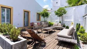 Una terraza en la azotea con mobiliario de madera, un sofá y plantas en macetas.