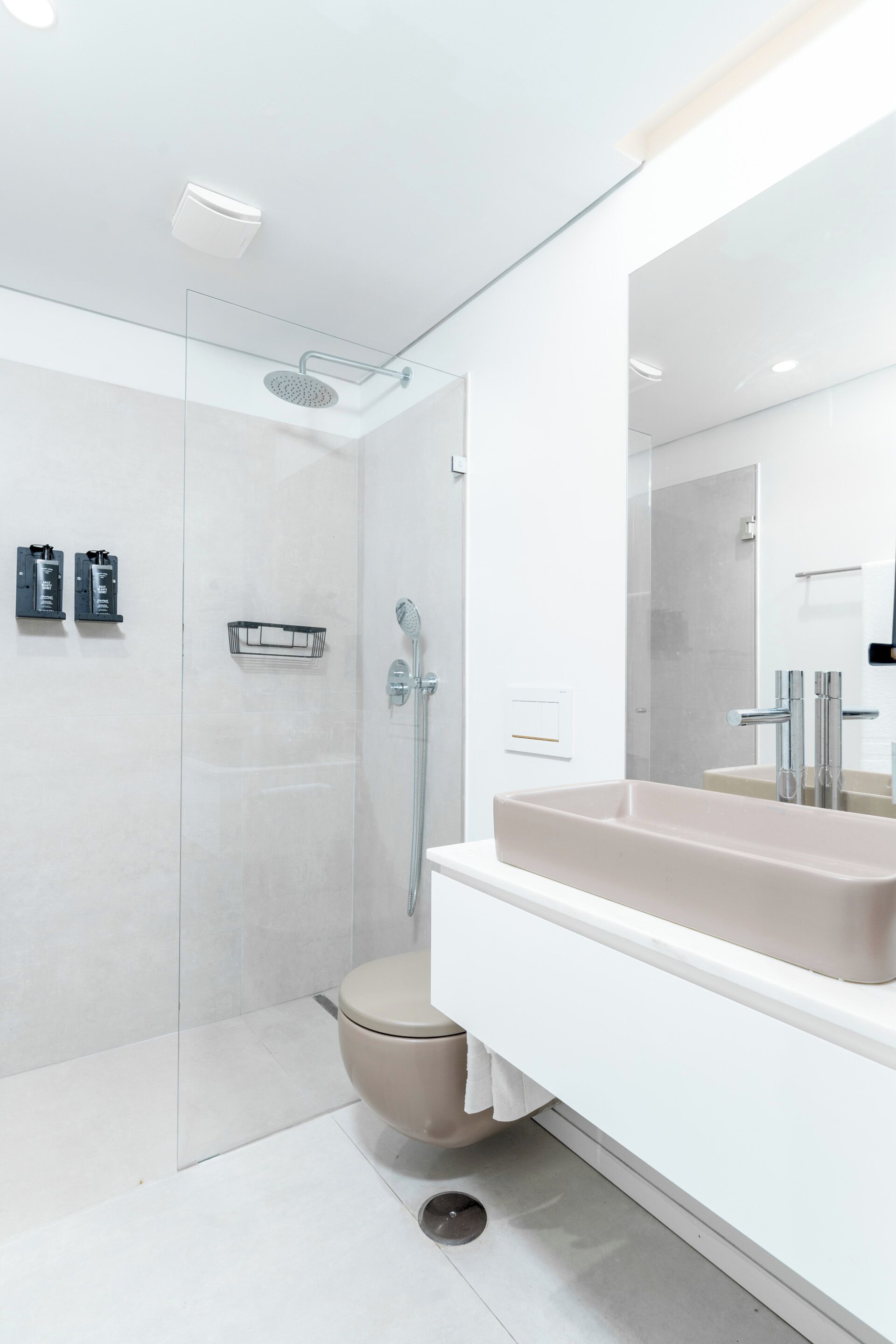 Un baño moderno con ducha envuelta en vidrio, inodoro color beige y tocador blanco con un espejo grande.