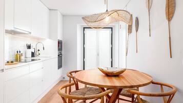 A modern kitchen with white cabinets, a round wooden dining table, and woven chairs.