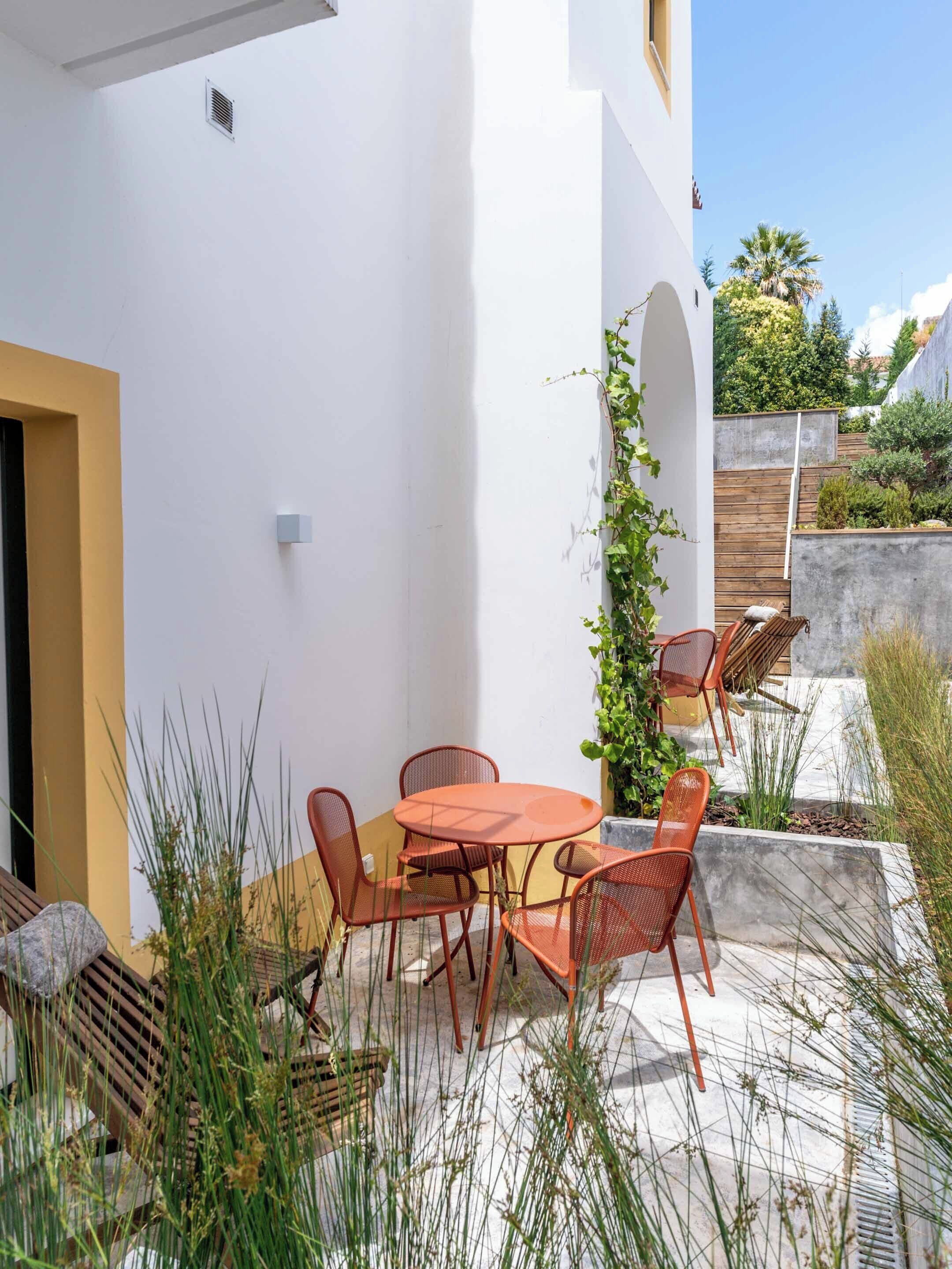A patio with a round table and four chairs, surrounded by plants and a concrete wall.