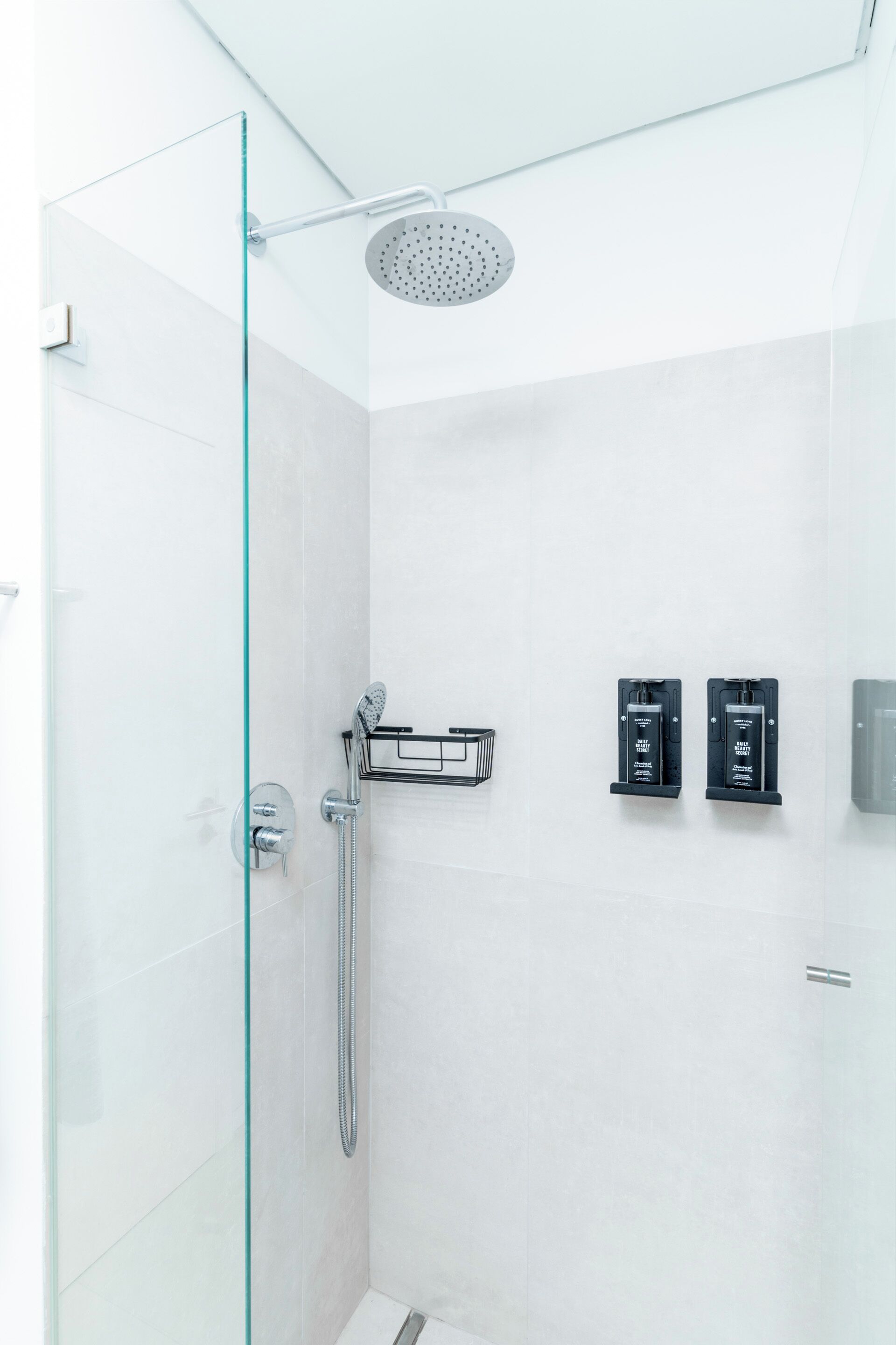 A modern shower with a glass door, a handheld showerhead, and two black soap dispensers on the wall.