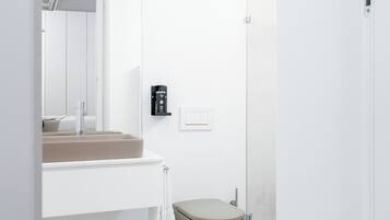 A modern bathroom with a white vanity, a toilet, and a light fixture.