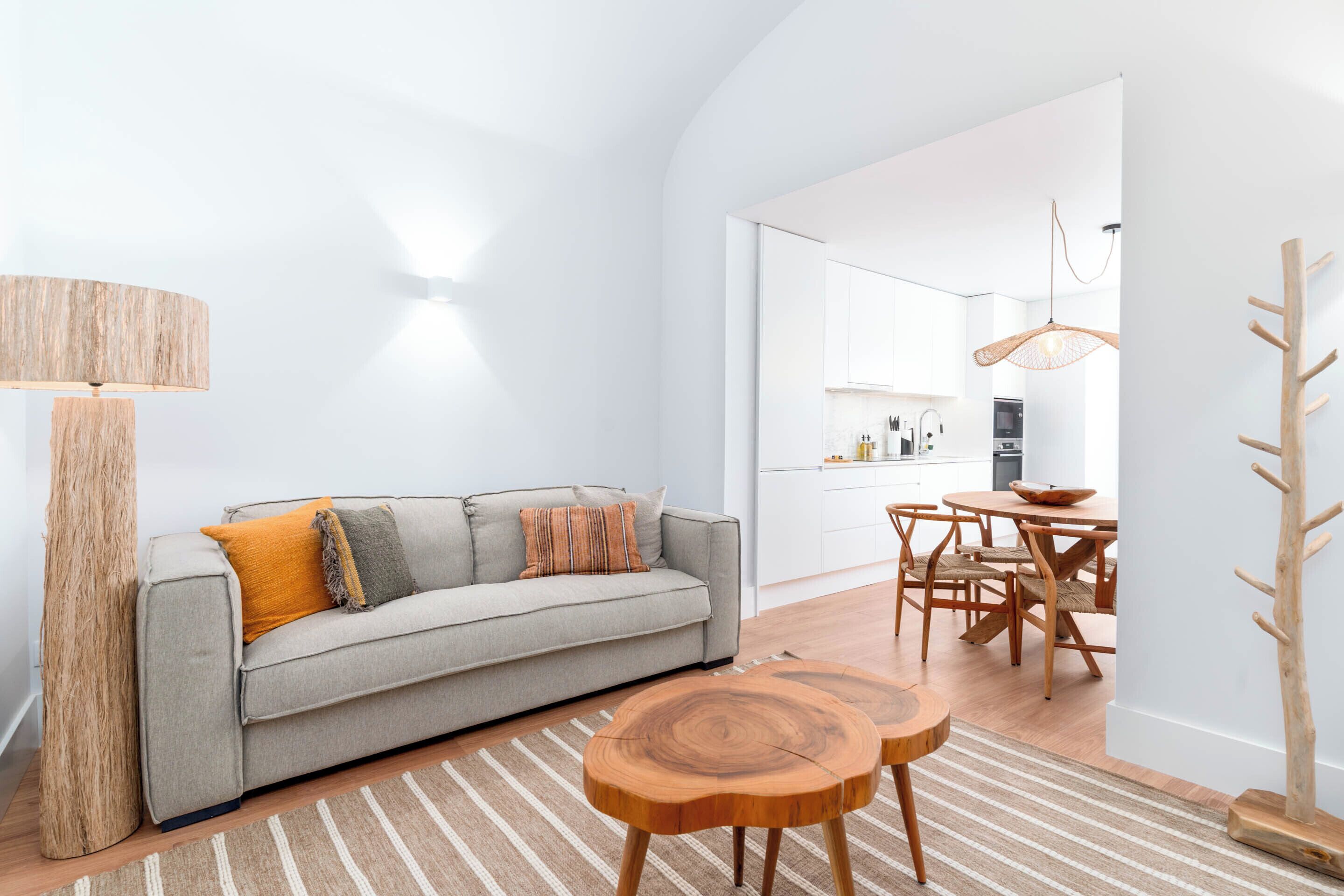 A modern living room with a sofa, wooden side tables, and a dining area with chairs and a table.