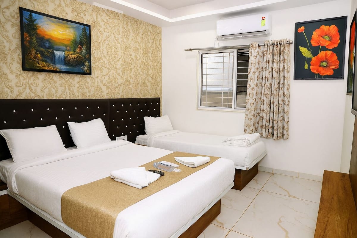 Une chambre d’hôtel avec un grand lit, un plus petit lit, une fenêtre avec des rideaux, un appareil de climatisation et des œuvres d’art accrochées aux murs.