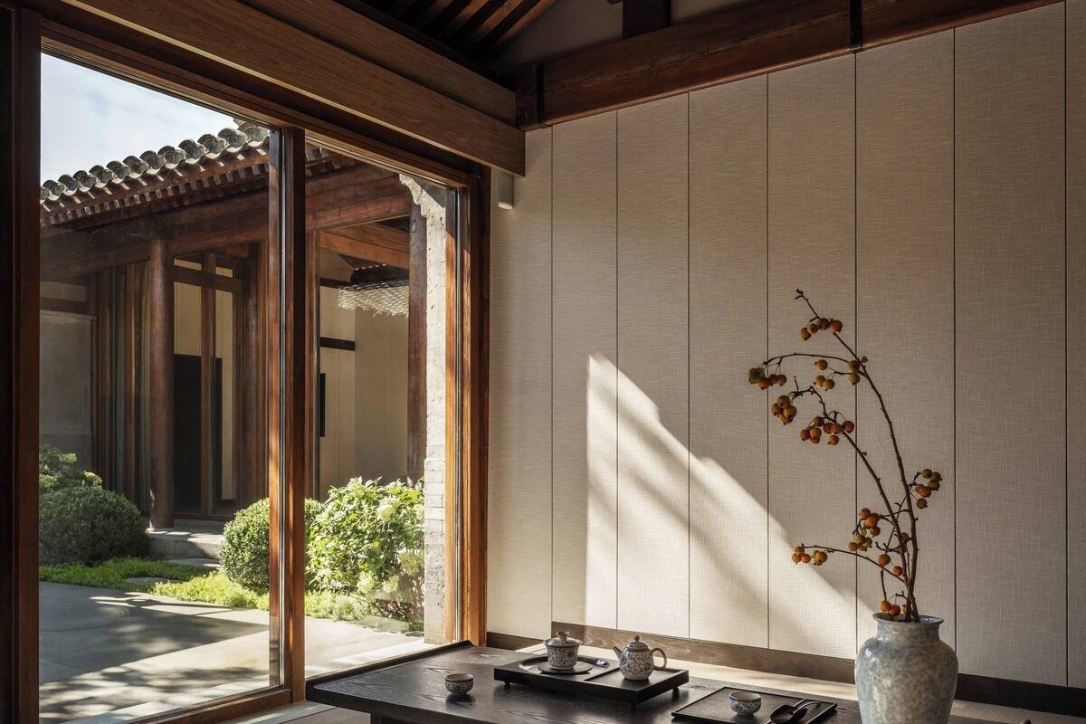 Una habitación japonesa tradicional con suelo de tatami, una mesa baja con juego de té y un jarrón con ramas.