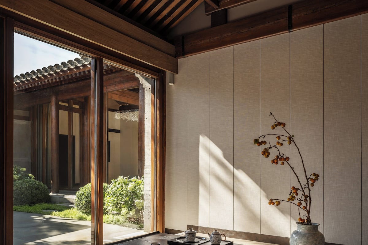 Una habitación japonesa tradicional con suelo de tatami, una mesa baja con juego de té y un jarrón con ramas.