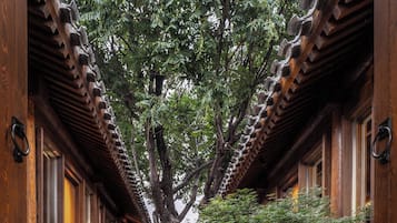 A traditional wooden building with a central courtyard, featuring a tree, seating area, and a small table with a candle.