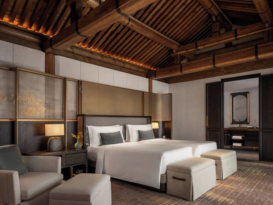 A modern hotel room with a large bed, a sofa, a desk, and a mirror.