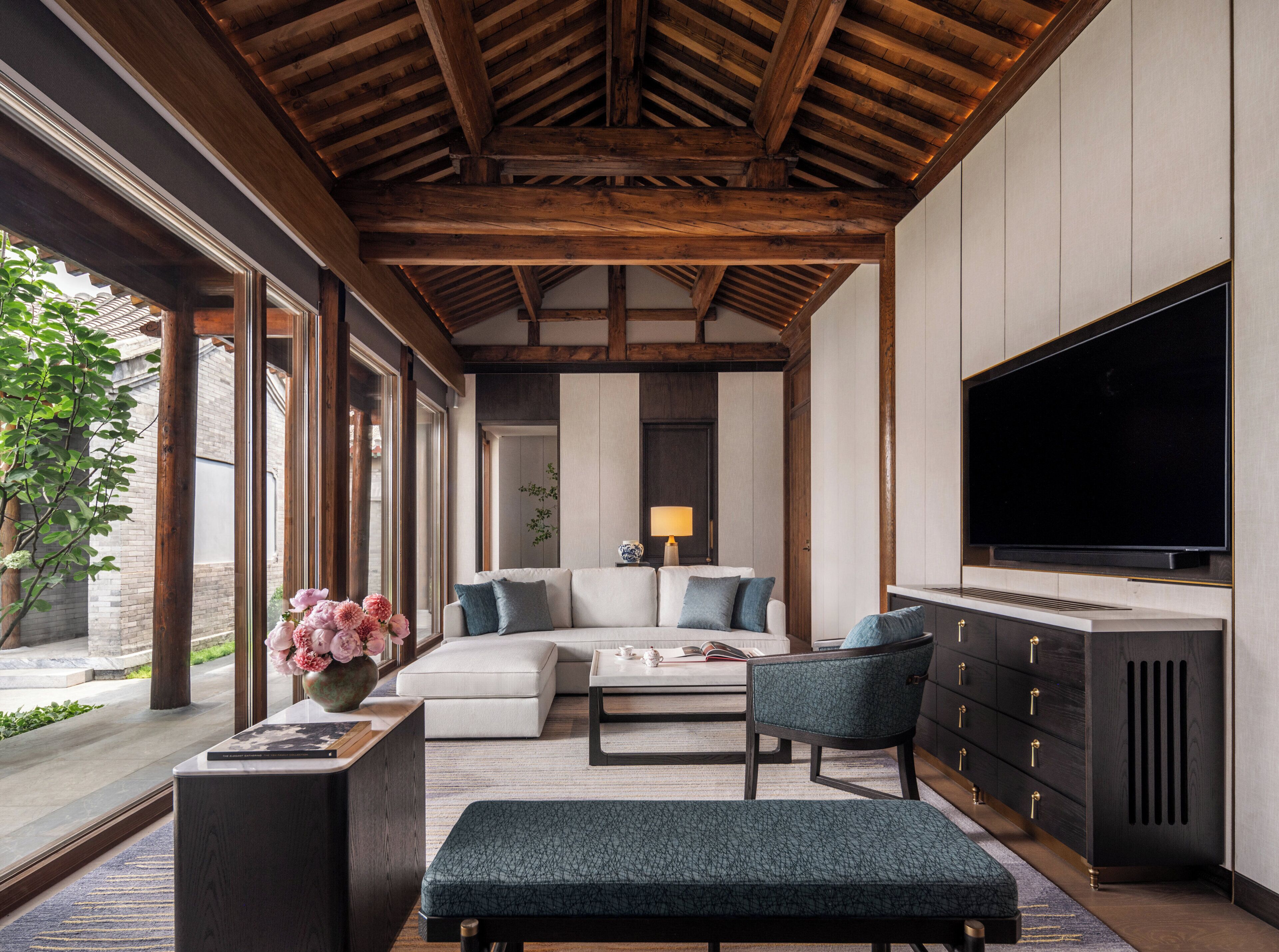 A modern living room with a wooden ceiling, a large flat-screen TV, a sofa, a coffee table, and a sideboard.