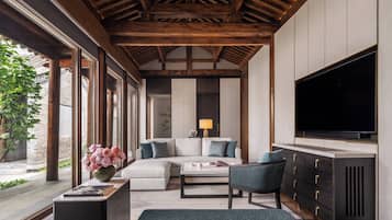 A modern living room with a wooden ceiling, a large flat-screen TV, a sofa, a coffee table, and a sideboard.