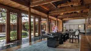 Una habitación amplia con techo alto, vigas de madera, una mesa grande, sillas y vistas al exterior.