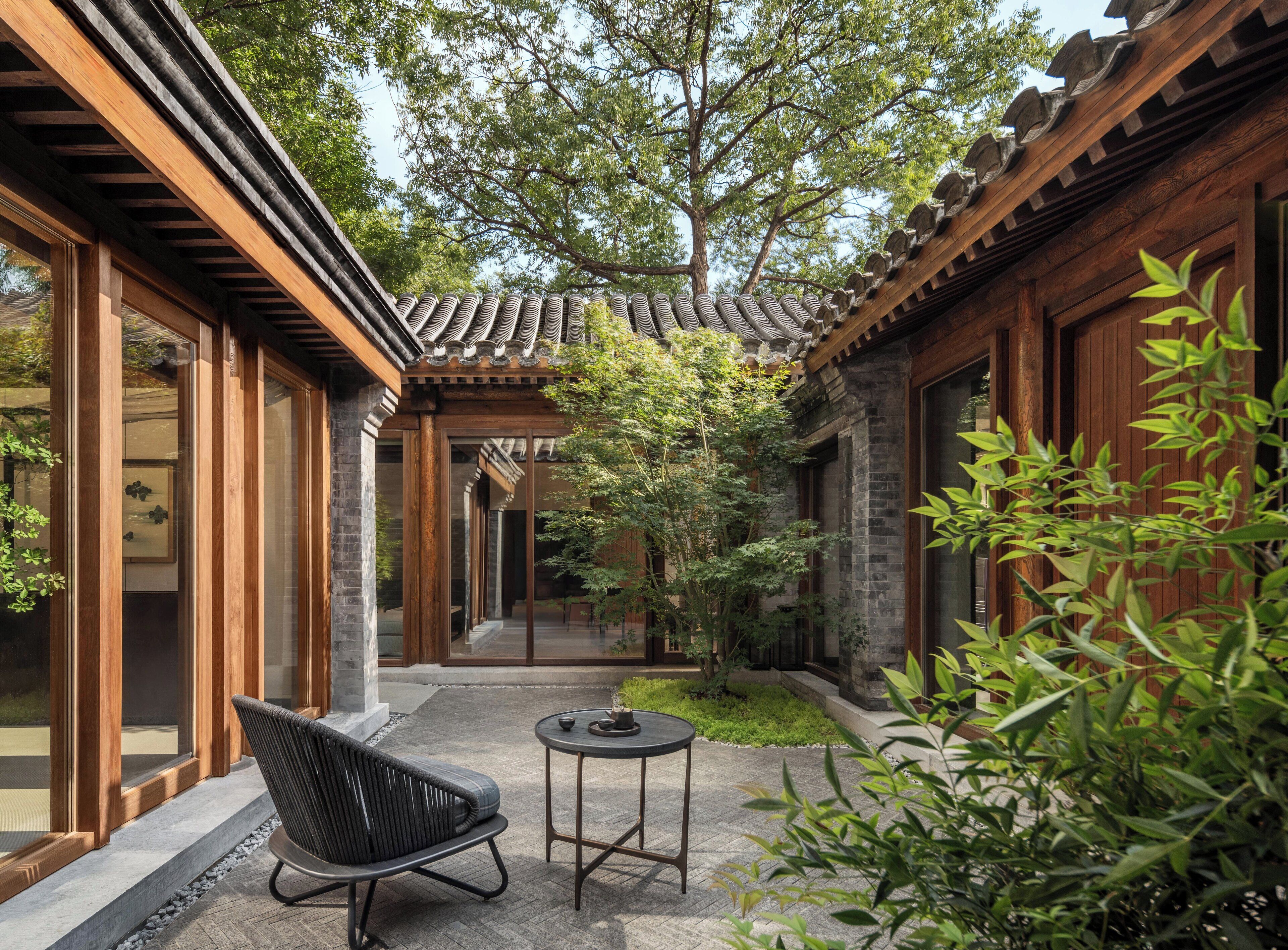 A traditional courtyard with wooden architecture, a seating area, and potted plants.