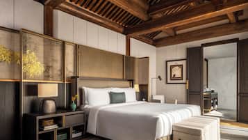 A modern bedroom with a large bed, wooden ceiling beams, a nightstand with a lamp, and a dresser.