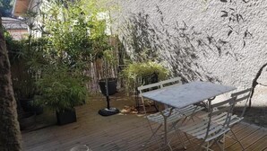 Une terrasse en bois avec une table et des chaises, entourée de plantes en pot et d’un mur de pierre.
