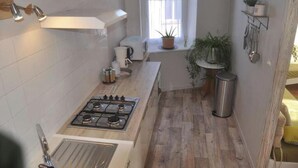 Une cuisine de taille réduite, équipée d’une cuisinière à gaz, de meubles blancs et d’une petite fenêtre.