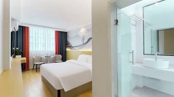 A hotel room with a bed, bedside table, chair, and a glass-enclosed bathroom with a sink and mirror.