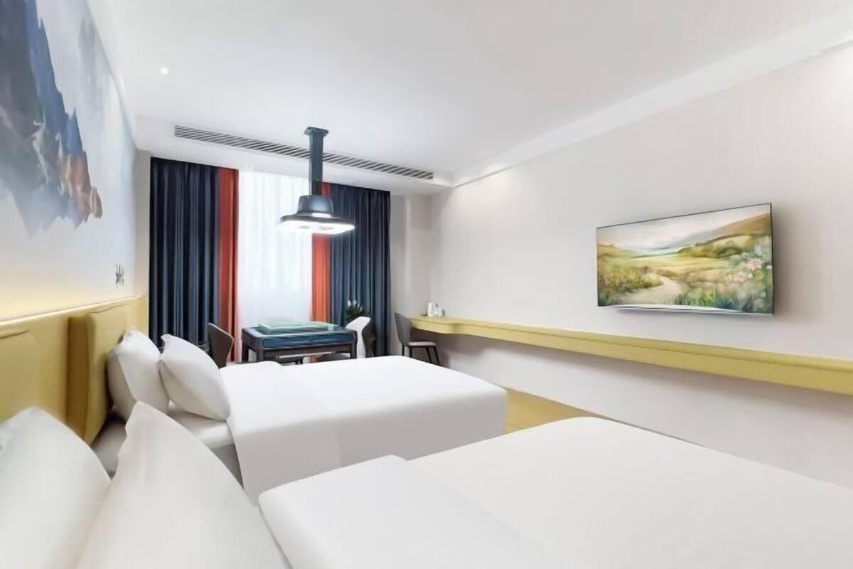 A hotel room with a bed, a desk, a chair, a painting on the wall, and a window with curtains.
