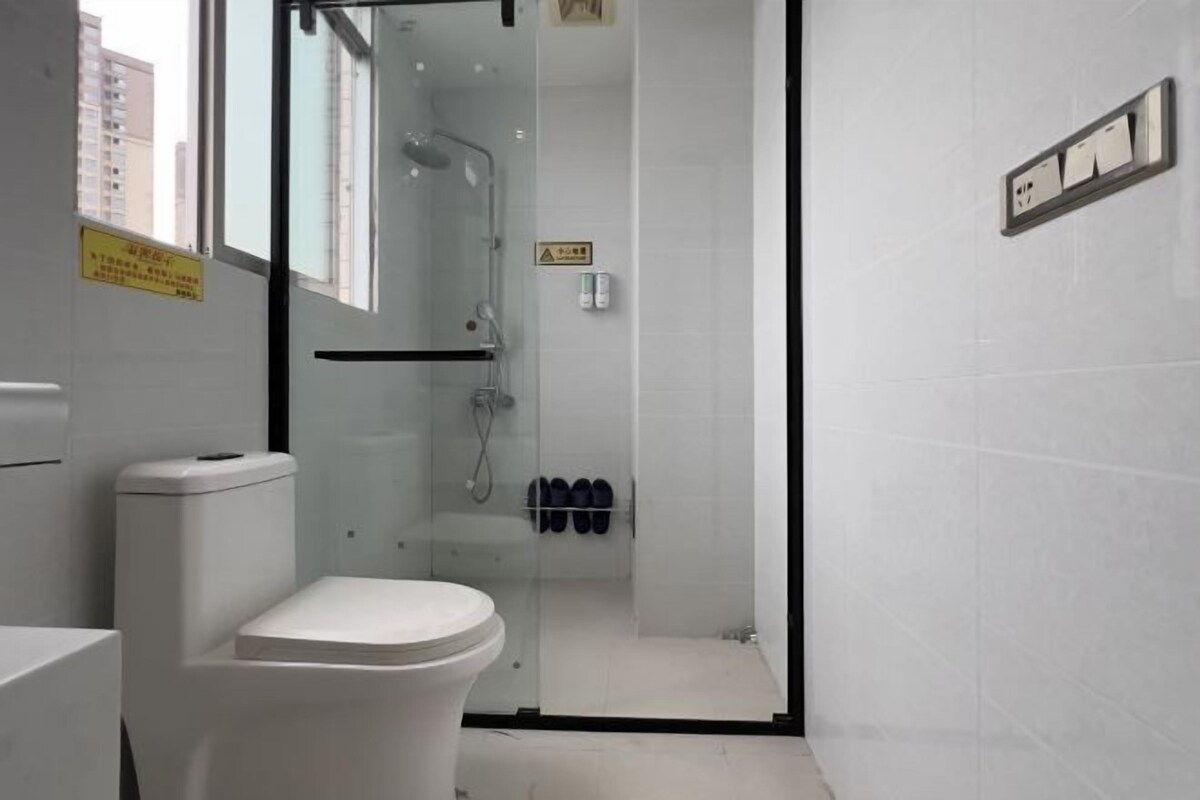 Un baño con inodoro, ducha con mampara de vidrio y un par de zapatos en la pared.
