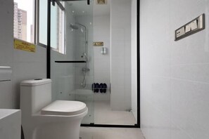 Un baño con inodoro, ducha con mampara de vidrio y un par de zapatos en la pared.