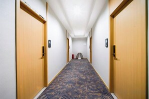 Un pasillo de hotel con puertas de madera, una alfombra estampada y un candelabro en el techo.