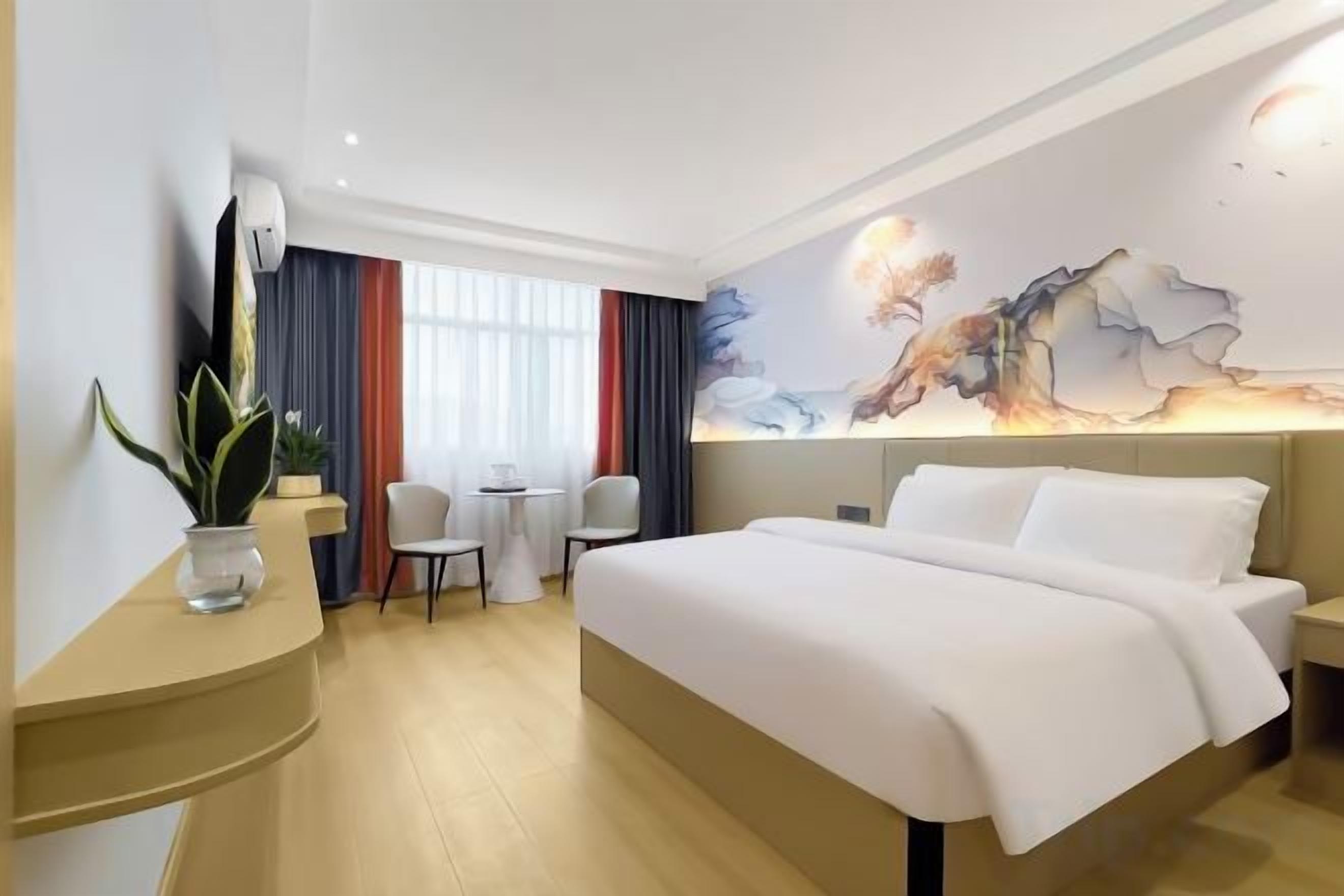 Habitación de hotel con cama, escritorio, silla, una mesita y ventana con cortinas.