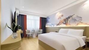 A hotel room with a bed, a desk, a chair, a small table, a potted plant, and a window with curtains. - afuerliansuozheyujiudian (Xiushan County)