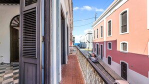 A narrow alleyway with a stone wall, a metal railing, and a row of colorful buildings.