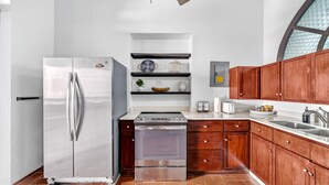 A kitchen with a stainless steel refrigerator, an oven, wooden cabinets, and a white countertop.