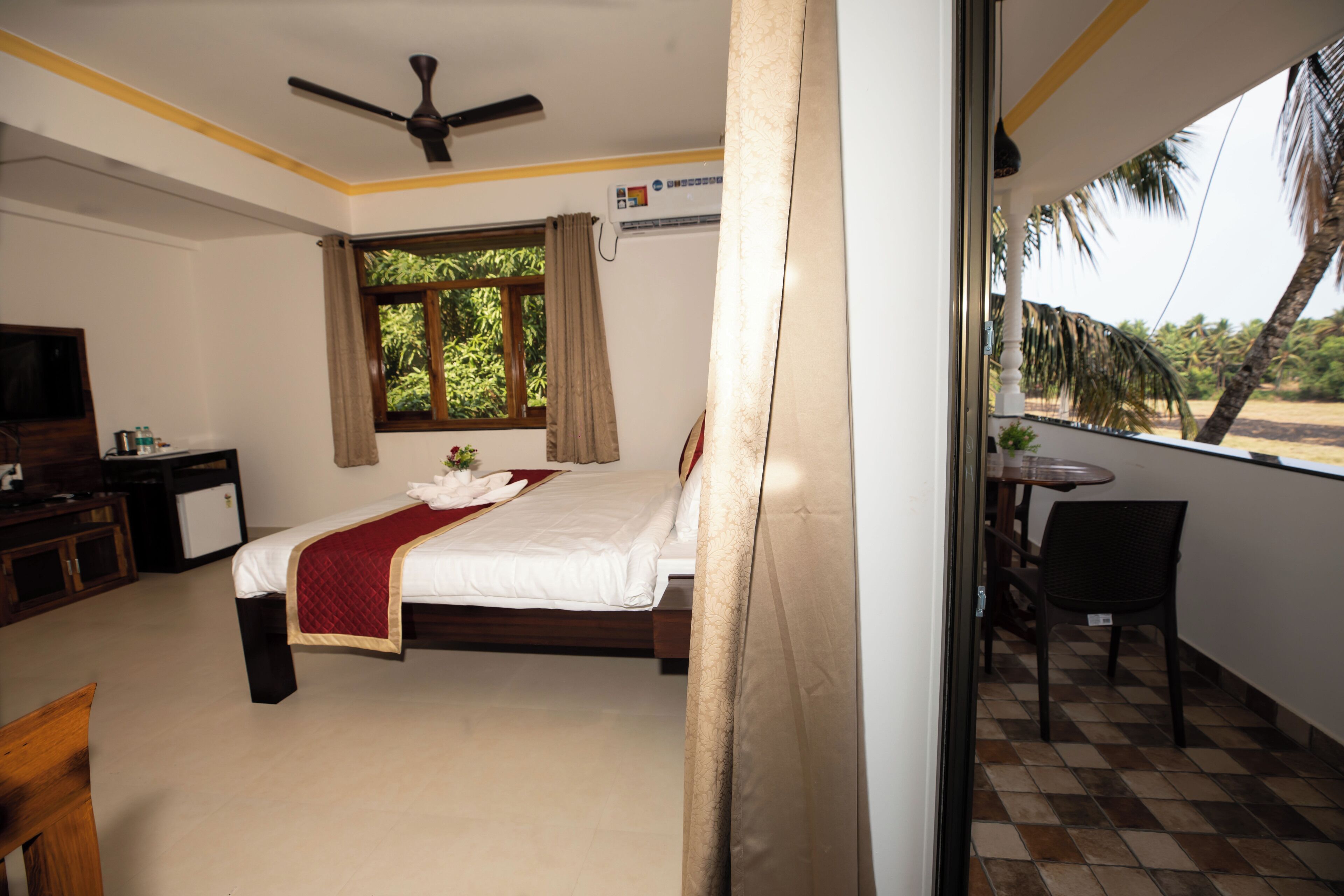 A hotel room with a bed, a desk, a chair, and a balcony with a view of palm trees.